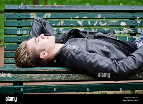 Handsome Blond Young Man Lying Down On Green Wooden Park Bench Stock