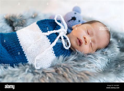 Newborn Baby Boy Sleeping And Swaddled In A Knit Wrap On A Bed Stock