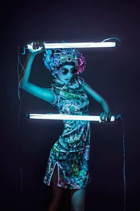 A Woman With Blue Makeup Holding Two Lights Up To Her Head And Wearing