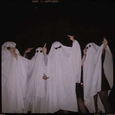 Four People Dressed In White Ghost Costumes Pointing At Something With