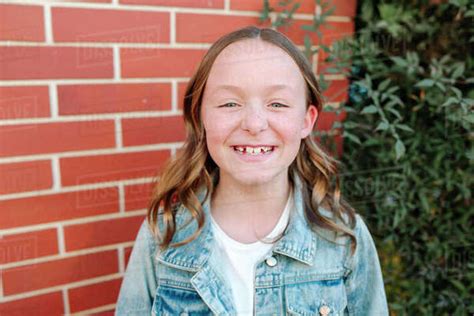 Happy Preteen Girl Wearing Denim Jacket By Brick Wall Stock Photo