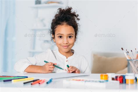 Adorable African American Kid Drawing With Felt Pens And Looking At