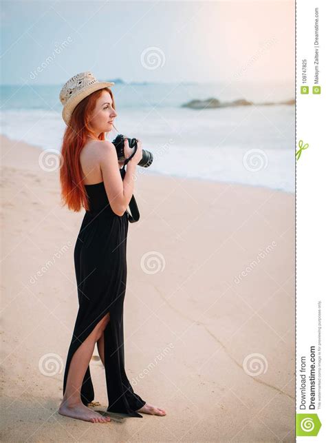 Young Woman Photographer Stands On The Beach With A Camera In Hands