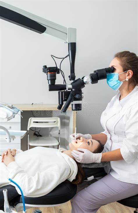 Female Dentist Using Dental Microscope Treating Patient Teeth At Dental
