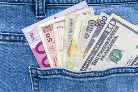 Multi Currency Banknotes In Back Pocket Of Blue Jeans On Orange Colour