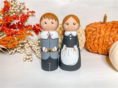 Two Wooden Dolls Are Sitting Next To Some Pumpkins