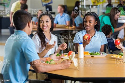 Diverse Teenage Friends Eat Lunch In School Cafeteria Stock Photo