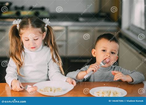 Boy And Girl Children In The Kitchen Eating Sausages With Pasta Is Very