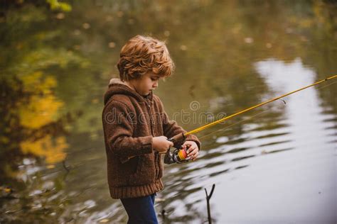 Little Fisherman Child Boy Fishing In Overalls From A Dock On Lake Or