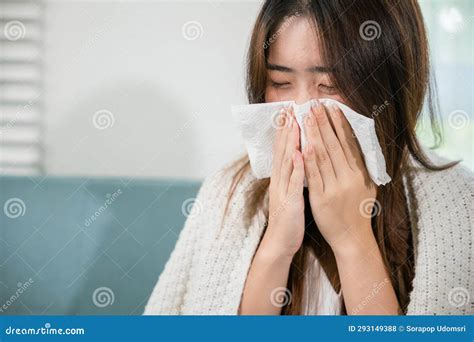 Sick Female Sitting Under Blanket On Sofa And Sneeze With Tissue Paper