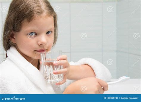 une fille en manteau blanc assise dans la salle de bain et tenant un verre d eau dans la main
