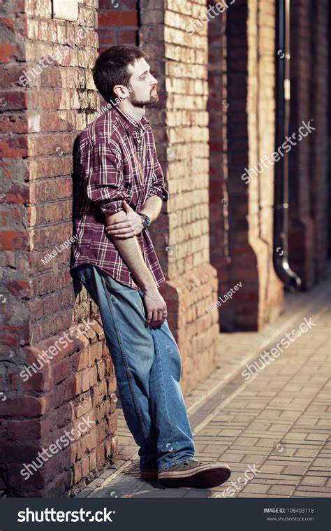 Pensive Young Man Leaning Against The Brick Wall And Waiting For