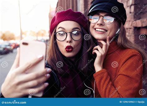 Two Joyful Cheerful Girls Taking A Selfie While Walking In The City Street Having Fun Stock