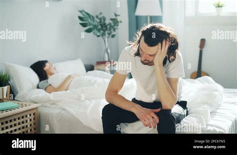 Unhappy Husband Sitting On Bed Touching Sad Face While Wife Sleeping At Home Stock Video Footage
