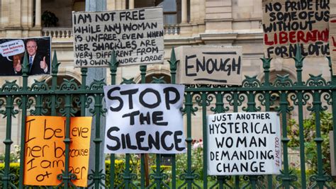 a number of signs with messages denouncing violence against women are taped to a metal fence