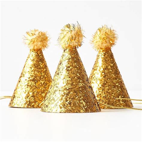 Three Gold Party Hats With Pom Poms On Them All Lined Up Against A