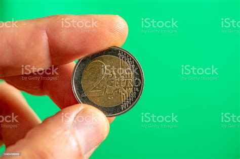 2 Euro Coin Face Held Between Thumb And Index Fingergreen Background