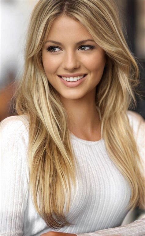 a beautiful blonde woman with long hair and blue eyes smiles at the camera while wearing a white
