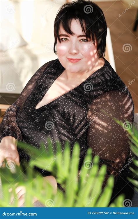 Plump Brunette With Short Hair Sits In A Chair Among The Branches Of A