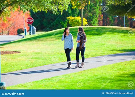 Two Teen Girls Talking While Walking Through Park In Autumn Stock Photo