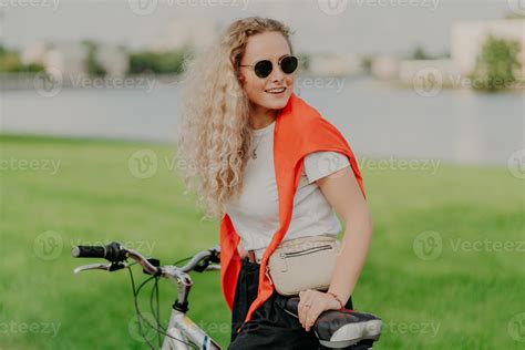 Photo Of Attractive Curly Haired Woman Focused Aside Wears Shades