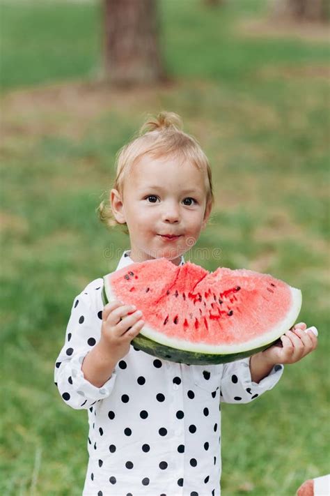 Cute Little Girl Eating Big Piece Of Watermelon On The Grass In