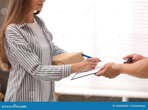 Woman Signing For Delivered Parcel At Home Courier Service Stock Photo