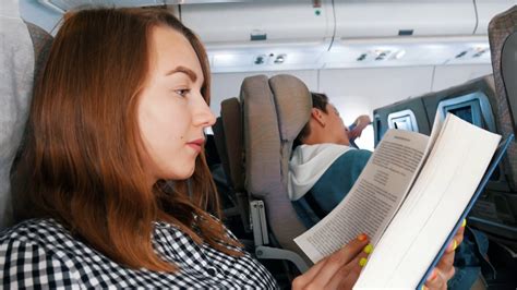 A Young Woman Sitting In The Airplane And Reading A Book Stock Video