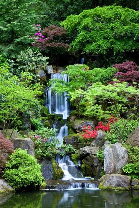 A Small Waterfall Surrounded By Lush Green Trees And Flowers In The