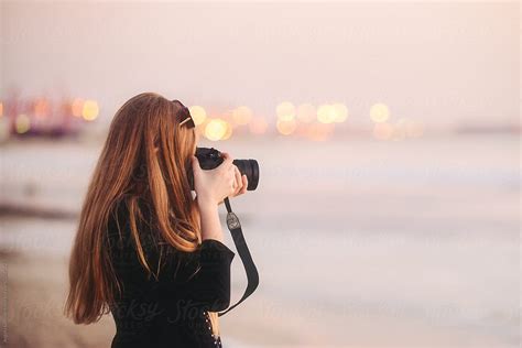 Teenage Girl Taking Photos At The Beach At Dusk With Out Of Focus Port