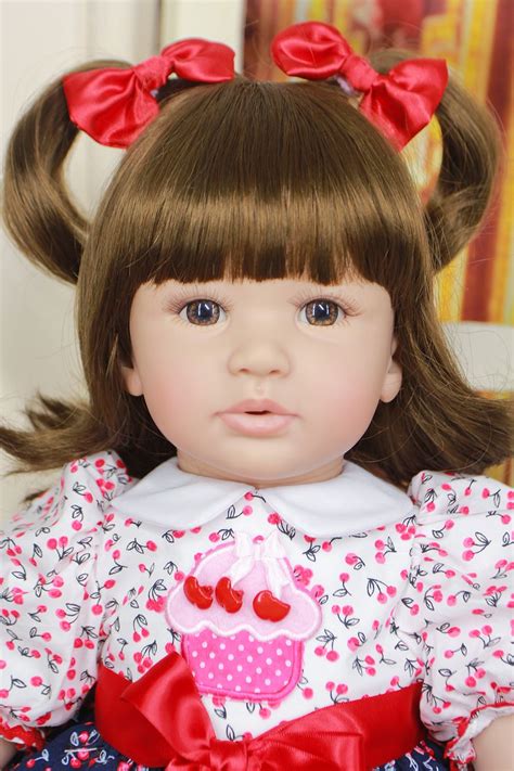 A Doll With Brown Hair Wearing A Pink Dress And Red Bow In Her Hair Is