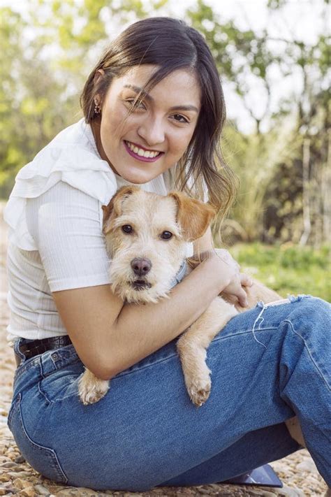 Young Woman Smiling And Hugging Her Dog While Sitting On A Pathway