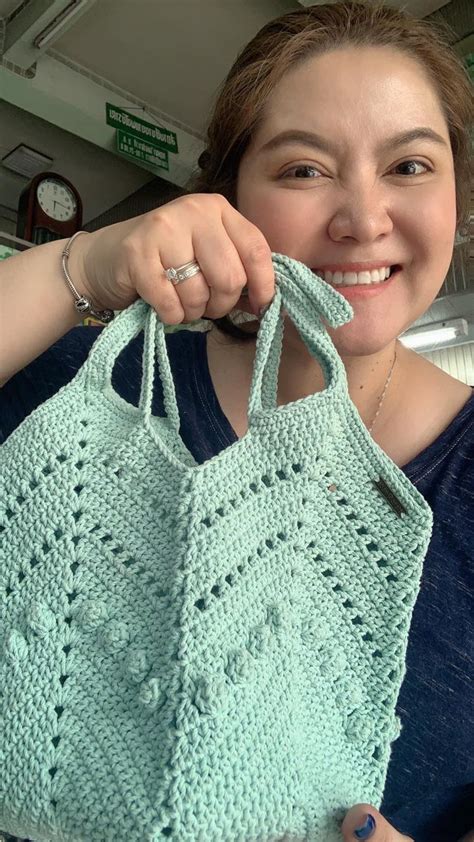 A Woman Holding Up A Green Crocheted Bag