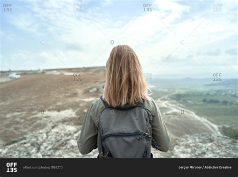 Back View Of Anonymous Female Backpacker Standing On Hill And Admiring
