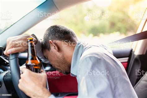 Drunk Asian Young Man Drives A Car With A Bottle Of Beer With Sunset