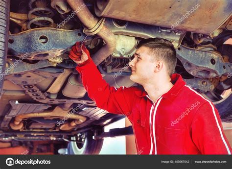 Young Auto Mechanic In Uniform Working Underneath A Lifted Car W Stock