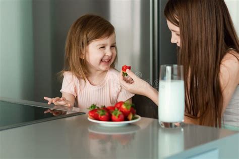 Two Girls Sisters Sitting At Kitchen Eating Strawberry Drinking Milk Stock Image Image Of