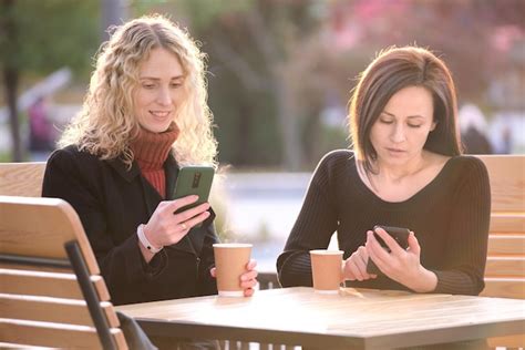 Premium Photo Two Distracted Female Friends Browsing Their Mobile Phones While Sitting