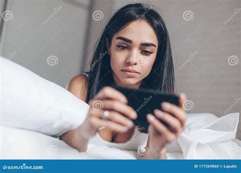 Serious Beautiful Woman Using Smartphone While Lying On Her Bed Smiling Brunette Girl Holding