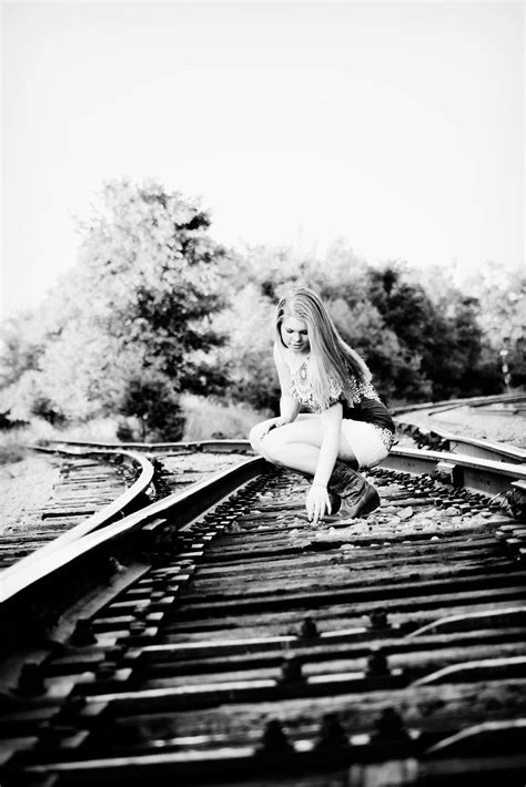 Black And White Photograph Of A Woman Sitting On Train Tracks With Trees In The Background