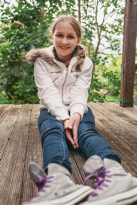 Tween Girl Sitting On A Wooden Deck Smiling To Camera By Stocksy