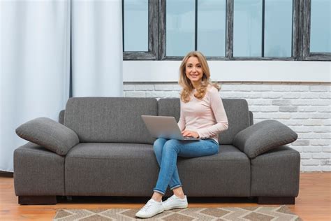 Young Woman Sitting On Sofa Using Laptop Looking At Camera Free Photo