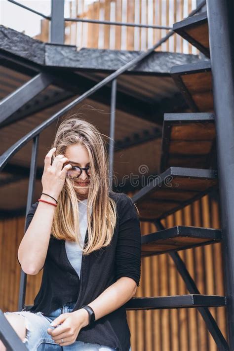Beautiful Girl With Long Hair And Glasses Sitting On Metal Stairs On