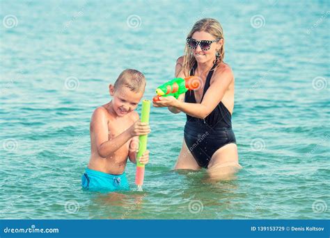 La Madre Ed Il Figlio Giocano Sulla Spiaggia Con Le Pistole Di Acqua Giovani Adulti Immagine