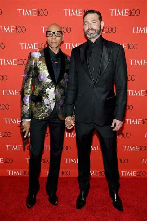 Two Men Standing Next To Each Other In Front Of A Time Sign On A Red Carpet
