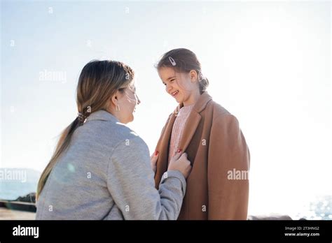 Two Cute Sisters Cuddle Outdoors Pretty Girls In Coats Against The Blue Sky Young Mom And