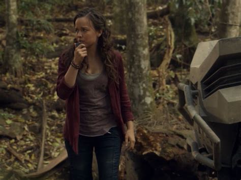 A Woman Standing In The Woods Next To A Vehicle And Talking On A Cell Phone