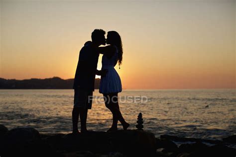 Silhouette Young Romantic Couple Kissing On Idyllic Beach At Sunset