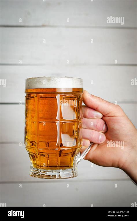Male Hand Holding A Full Beer Mug On White Wooden Background Toned