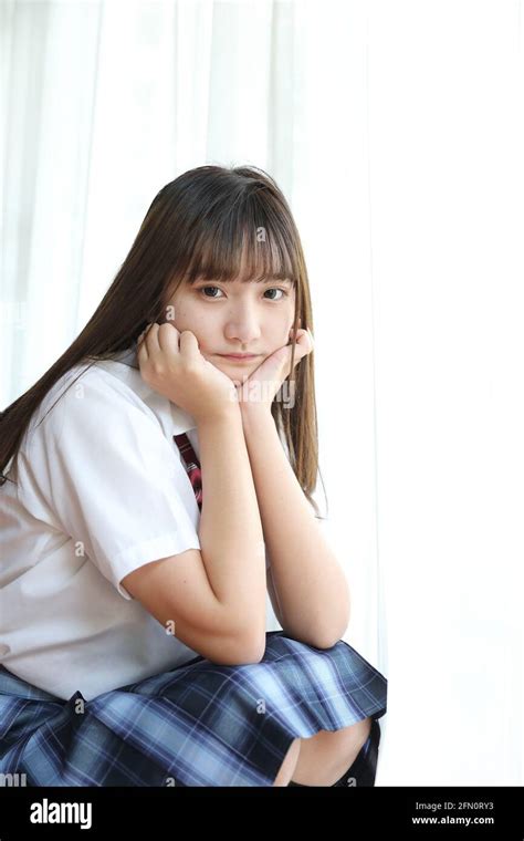 portrait japanese school girl uniform sitting and look at camera in white tone bed room stock